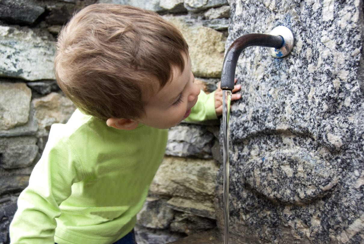 A young child is playing with the water from a faucet.