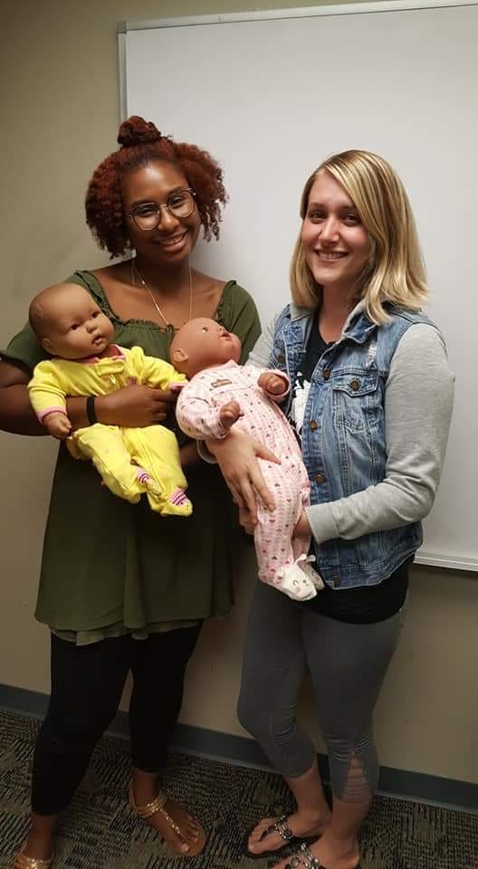 Two women holding baby dolls and a stuffed animal.