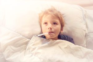 Child in bed with thermometer, looking unwell.