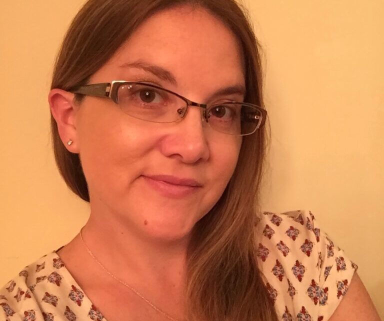 Woman wearing glasses and patterned blouse, smiling.